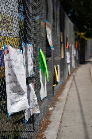 Multiple signs made by teachers taped to school fence during distance learning