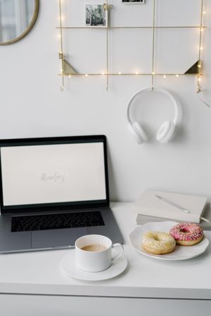 Laptop beside cup of coffee and donuts on a desk table