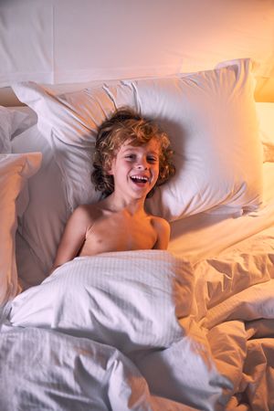 Merry boy lying in bed in evening