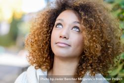 Woman with curly hair standing outside looking up 0L8qV0