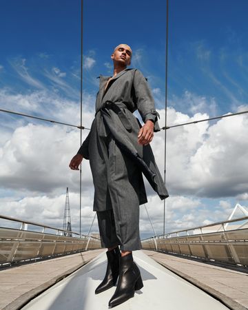 Stylish young man in gray coat and pants on bridge