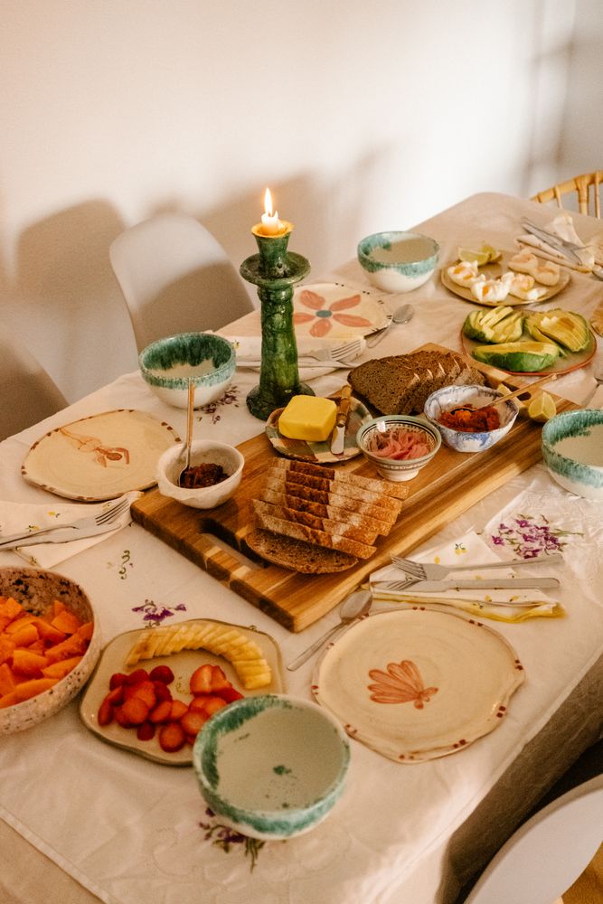 Casually set breakfast table, with bread, fruits, eggs and avocado