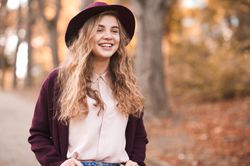 Happy teenage girl in purple coat with hat standing near fallen autumn tree leaves