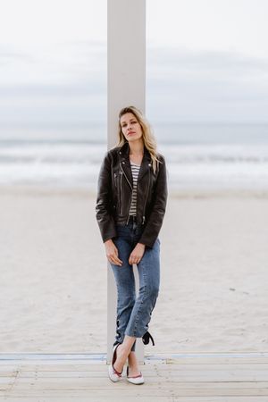 Smiling trendy woman leaning on white pillar on seashore
