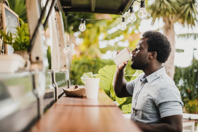 Young Black man eating and drinking in food truck counter outdoor in city park - Focus on face