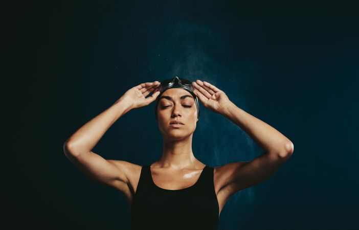 Professional female swimmer with eyes closed on dark background