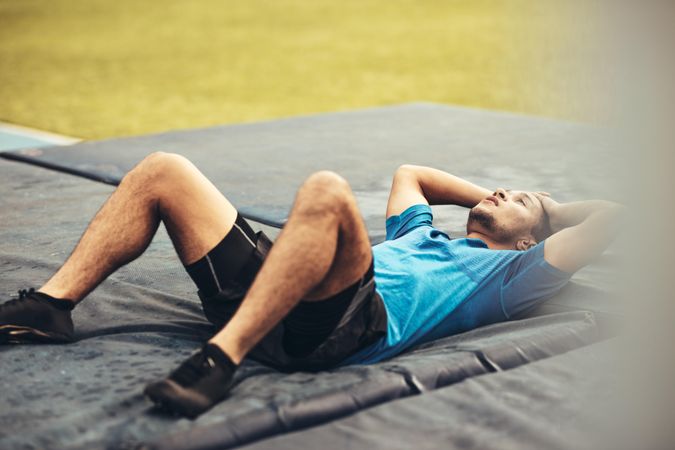Athlete lying on high jump landing mat looking tired