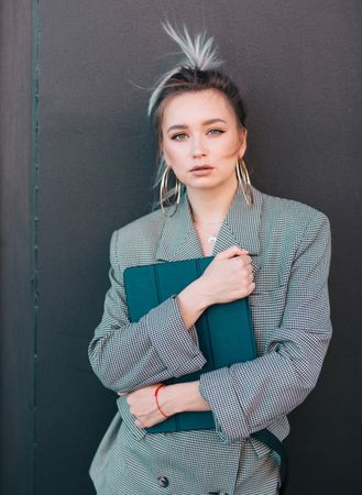 Stylish businesswoman with laptop leaning on wall