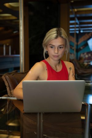 Young woman in red tank top working on laptop in a coffee shop