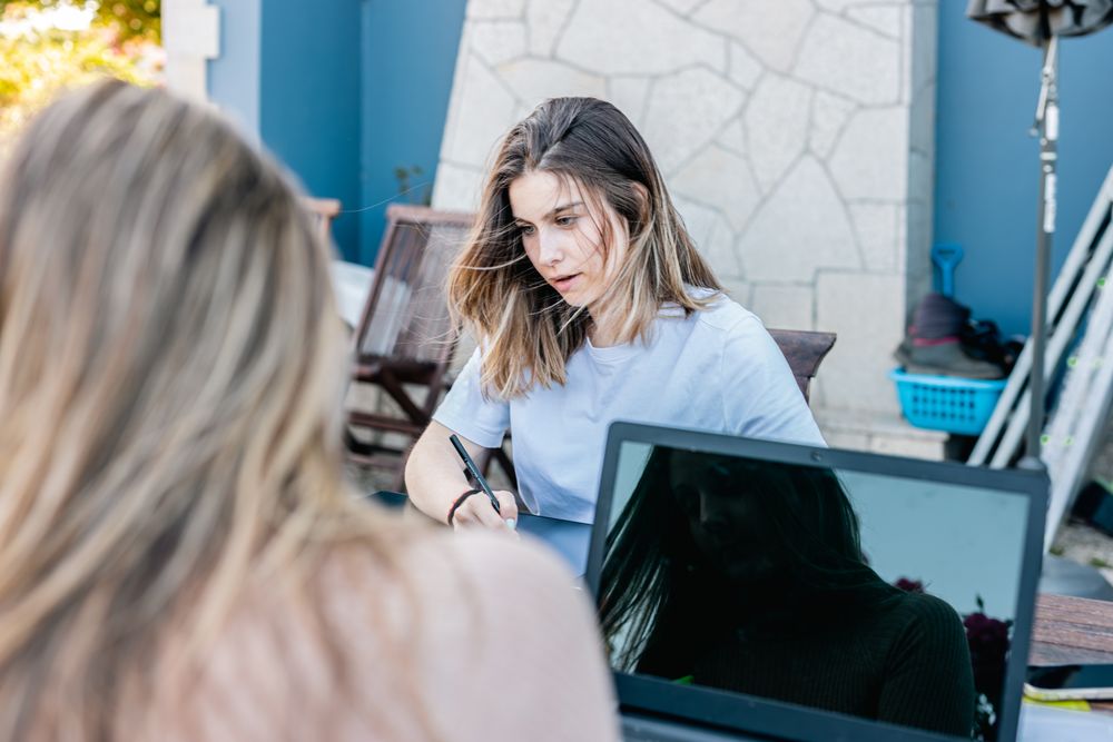 Young joyful woman working on the laptop chatting with her coworkers on a break on terrace outdoors.