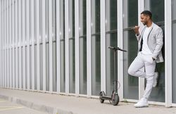 Elegant Black man talking smartphone leaning building