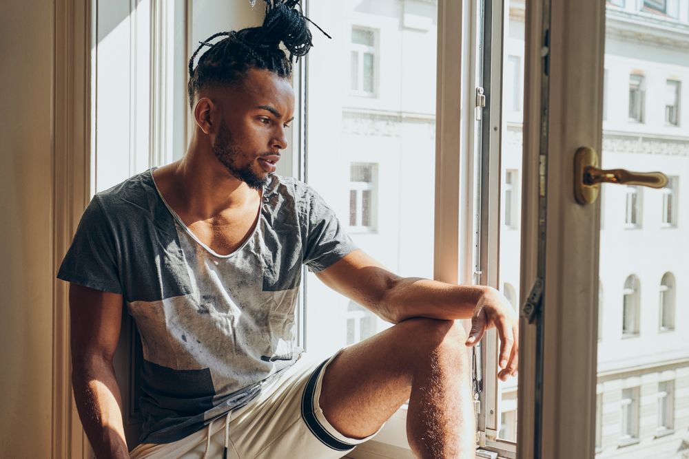 Thoughtful Black male sitting on windowsill