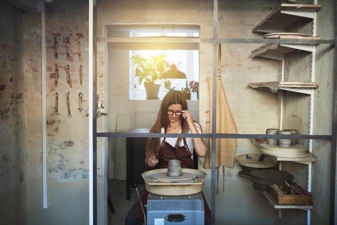 Contemplative woman in leather apron looking at clay on a wheel