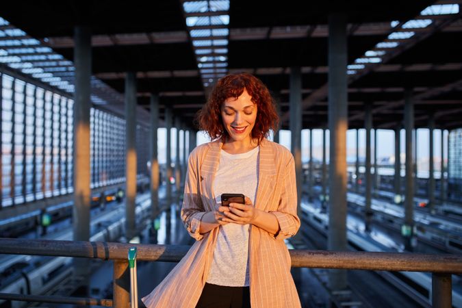 Smiling young woman browsing phone at station