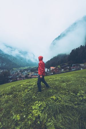 Side view of man in red jacket walking on green grass field near village in Switzerland