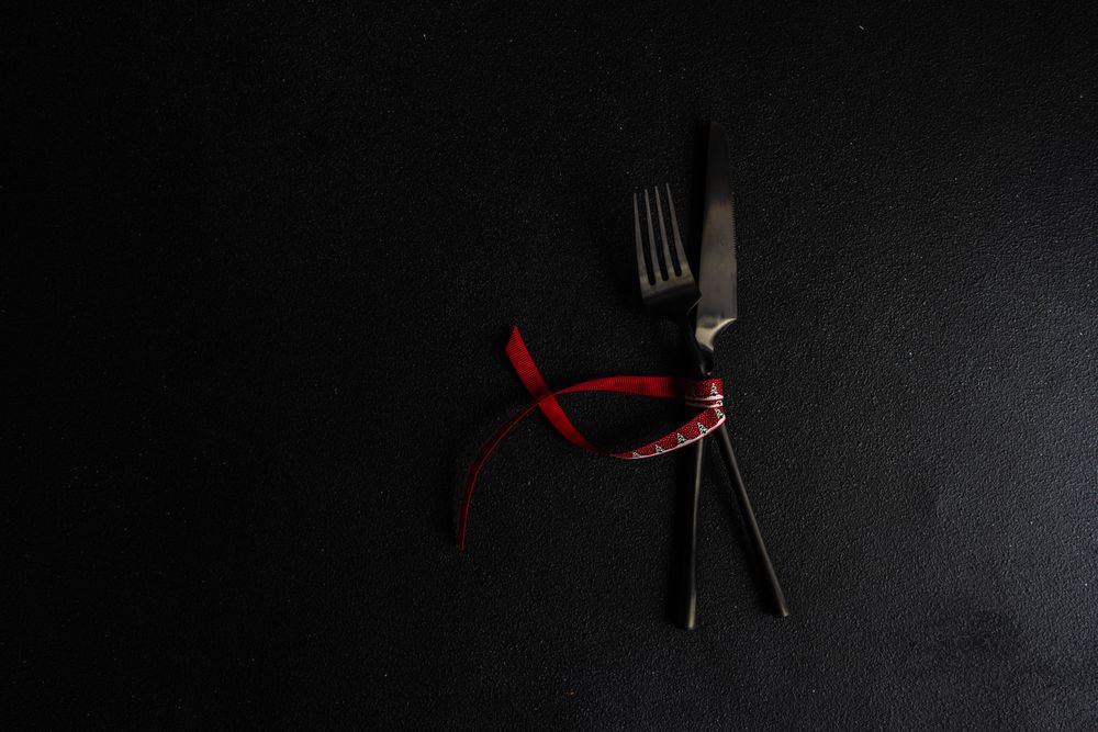 Dark knife and fork on dark background tied with bright red ribbon