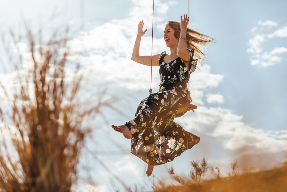 Happy woman enjoying on a swing at sunset