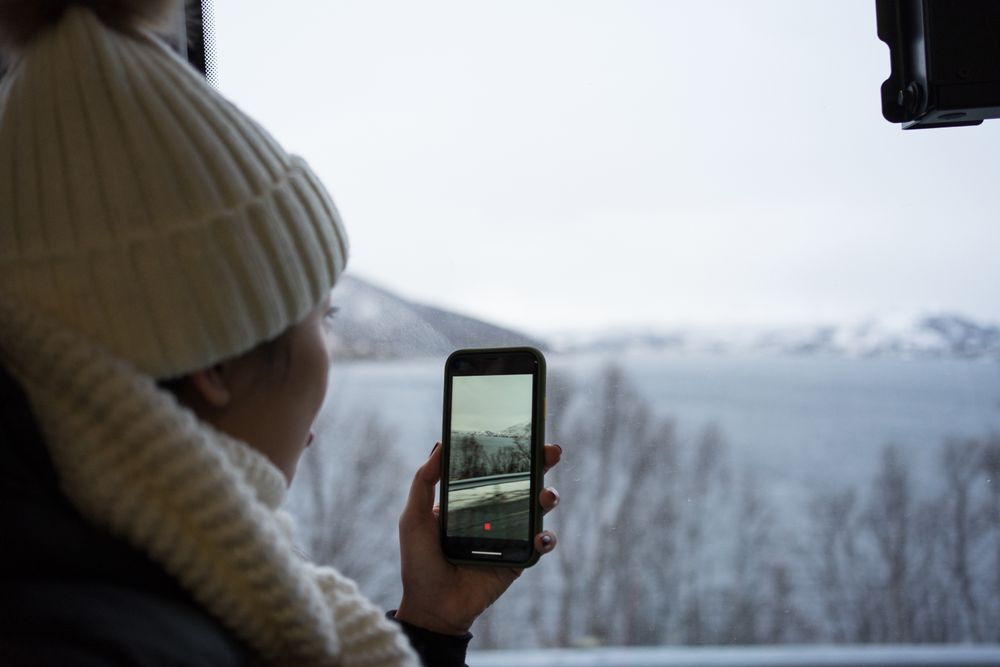 Calm woman recording video with smartphone of wintry scenery while looking out window