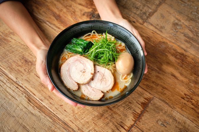 Crop person with bowl of ramen soup on wooden table