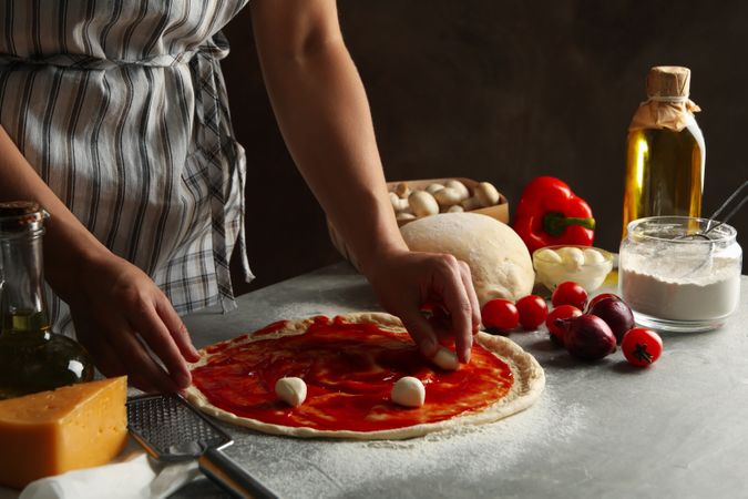 Woman cooking pizza on gray table with ingredients