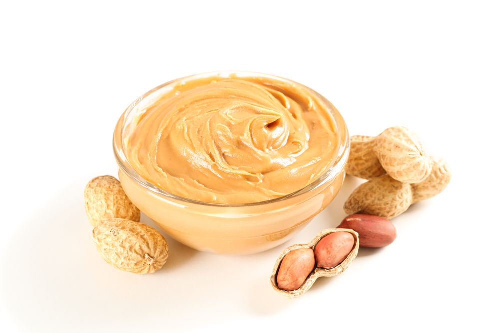 Creamy peanut butter in glass bowl and peanut isolated on light background. A traditional product of American cuisine