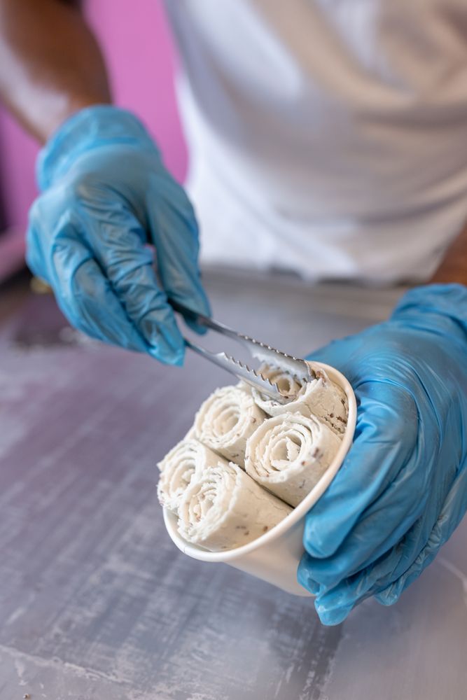 A worker is putting chocolate ice cream rolls in a tub using tongs and latex gloves