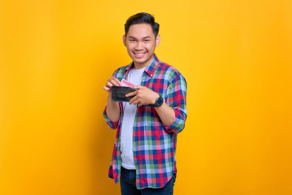 Asian man smiling while taking cash out of his wallet