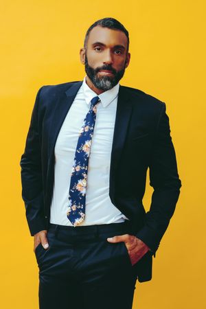 Confident Black male in navy suit with floral tie in yellow studio