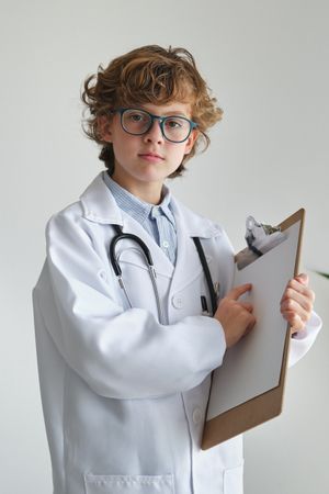 Boy in medical robe showing blank paper on clipboard