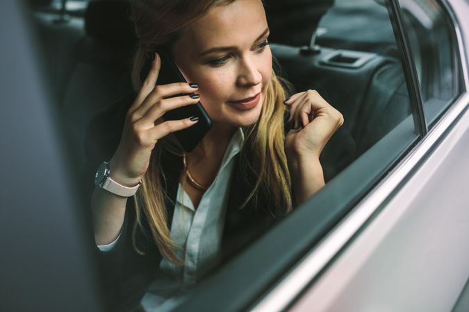 Young businesswoman talking on the cellphone while sitting in back seat of a car