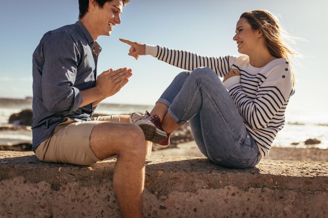 Happy couple playing a game sitting on a concrete wall near the sea shore