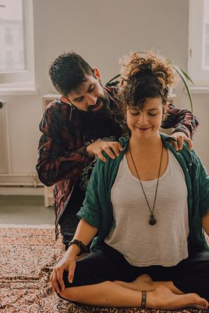 Man rubbing shoulders of joyful woman resting on floor at home