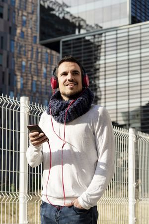 Young man listening to music on headphones while holding a mobile phone walking outdoor