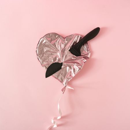 Pink foil heart balloon pierced with plastic knife on pink background