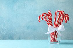 Candy canes in glass jar on blue background, space for text