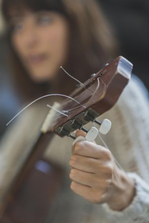 Female hands tuning strings of a guitar, vertical