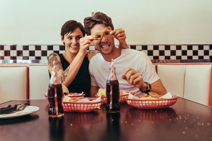 Woman sitting at a restaurant with man and having fun holding biscuit rings to his eyes