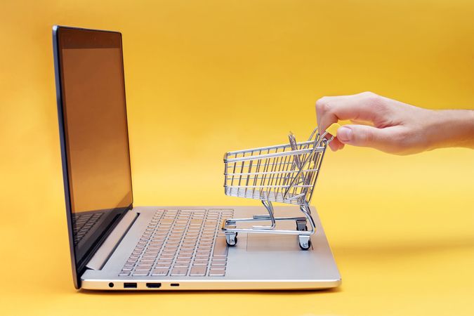 Laptop with Mini Shopping Cart Representing Online Shopping on Yellow Background