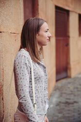 Woman in cardigan and satchel bag standing outside leaning on stone wall