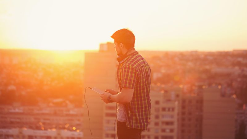 Male holding digital tablet with headphones on roof at dusk