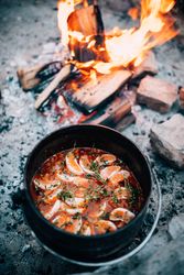 Pot of soup sitting next to an open camp fire
