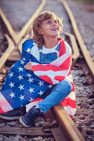 Smiling boy looking up on railroad switch with American flag