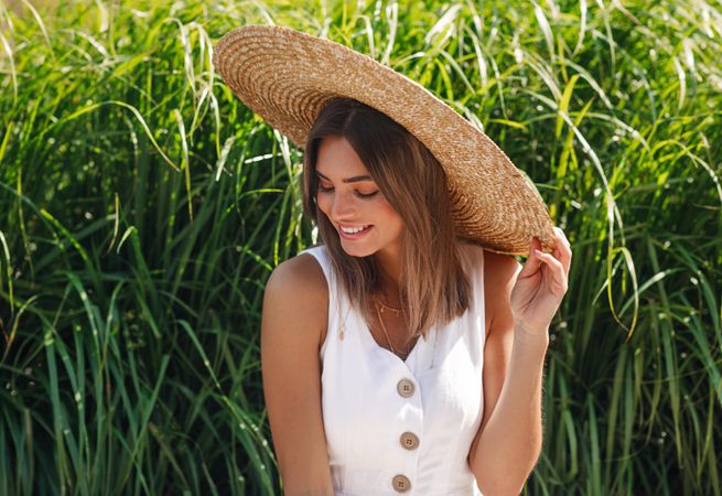 Woman sitting in front of long grass looking down while holding her straw hat