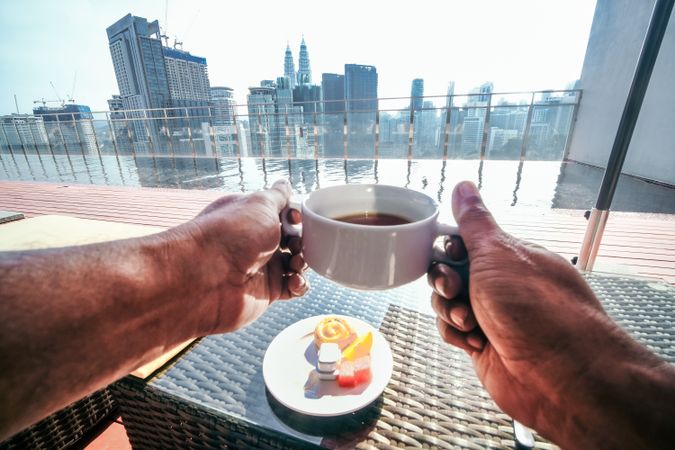 Person’s hands holding coffee cup over looking city