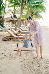 Happy child swinging with mother support while resting on ocean beach