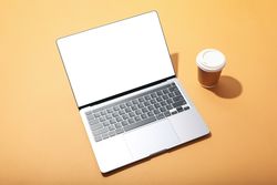 Top view of laptop with mockup screen and to go coffee on light orange desk
