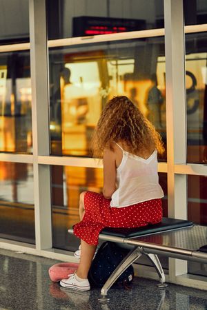 Stylish cheerful woman sitting on metal bench in glass hallway of airport in Texas