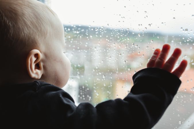 Anonymous baby looking out wet window