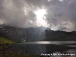 Sunrays out of cloudy sky on calm lake near mountains bYrv10