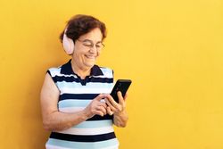 Older woman using smartphone and listening to music with headphones
